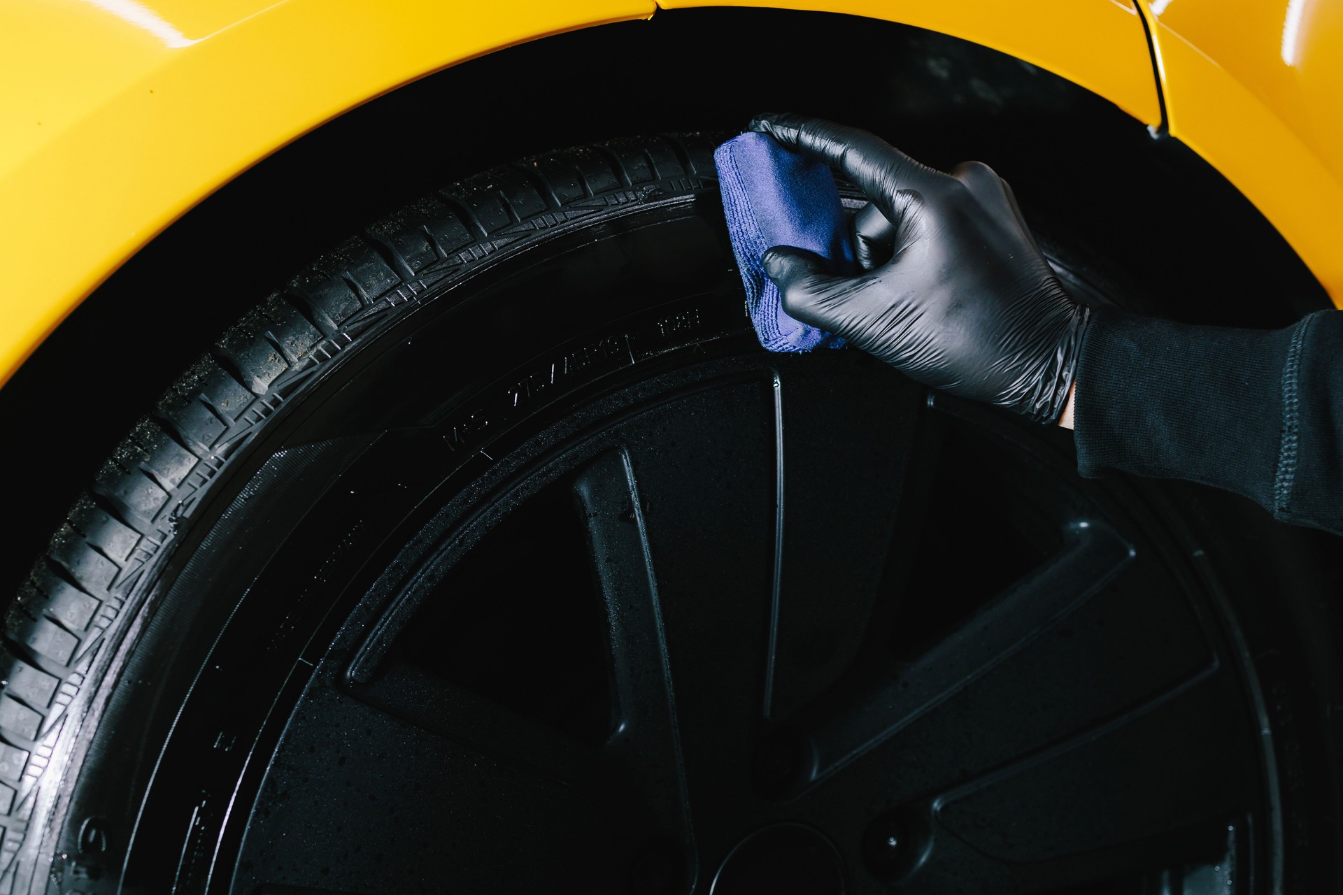 Mechanic applies a product to a black tire using a blue applicator. Blackening of tire wheel of car using sponge with chemical blackening of rubber in detailing auto service.